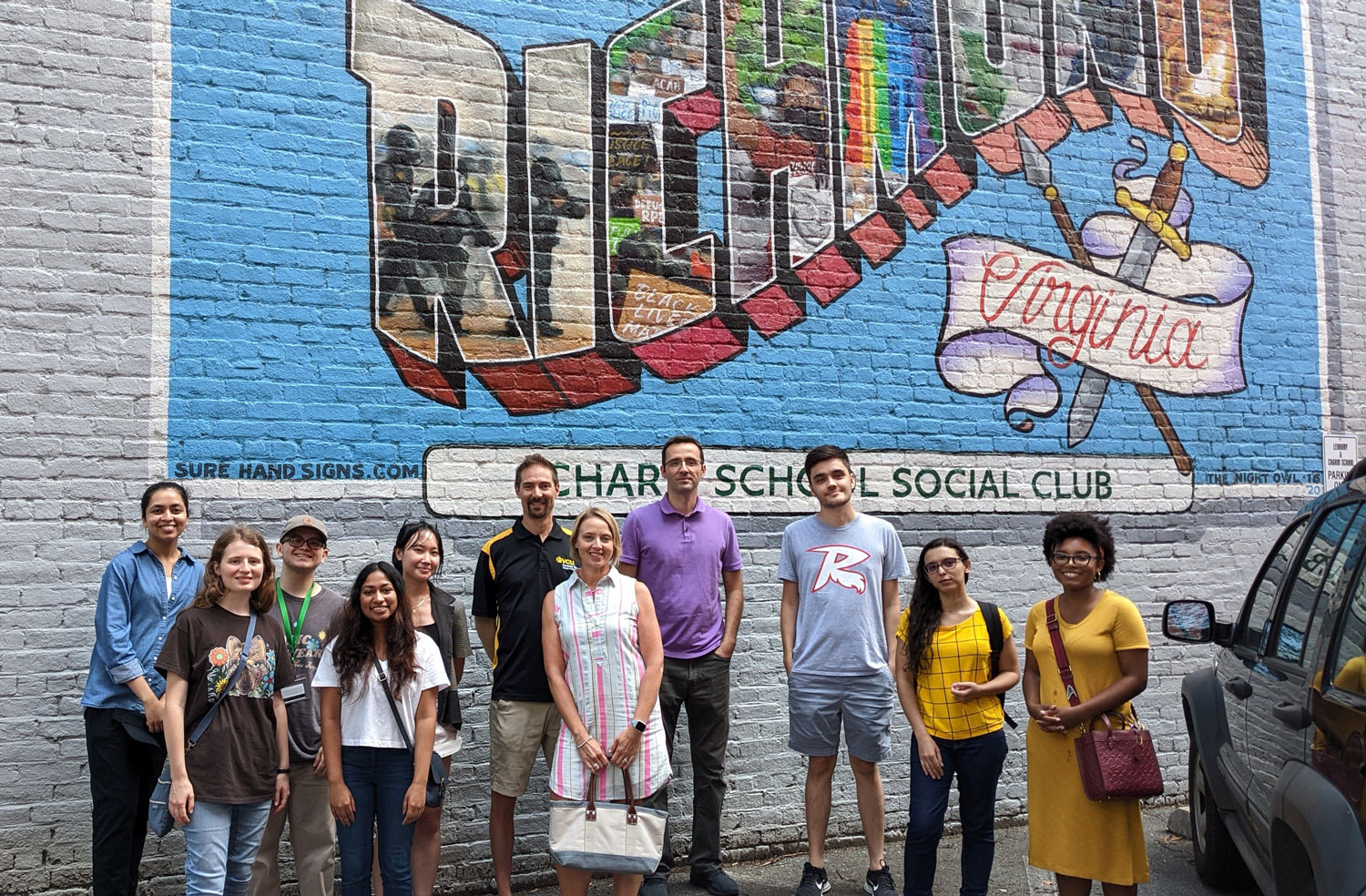 Summer REU students standing in front of a mural outside Charm School Social Club
