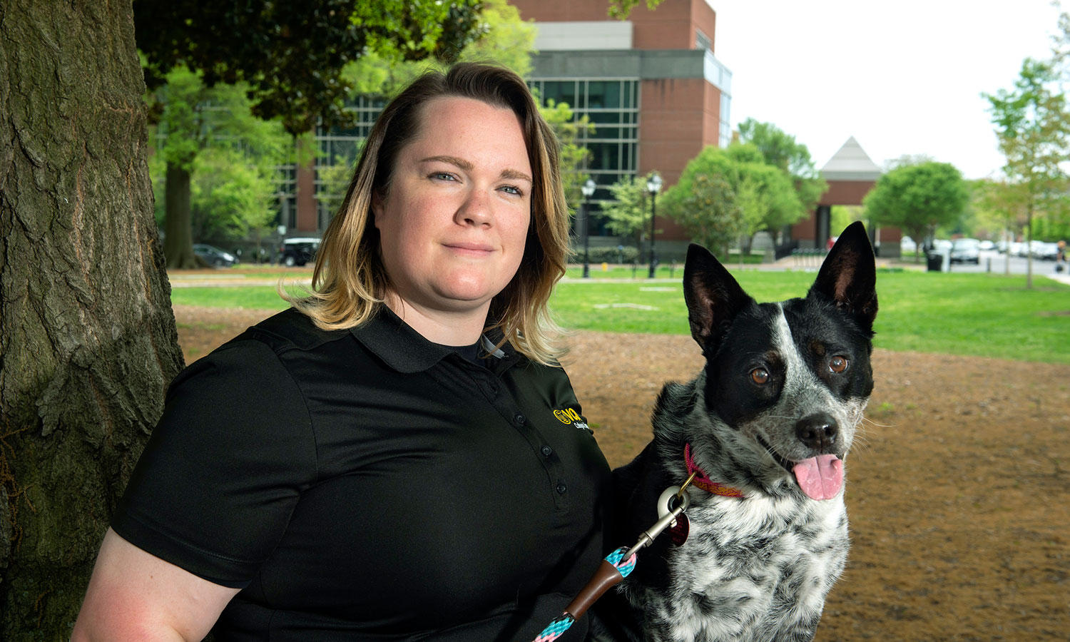 Ashley Lawrence and her dog, Roxie, in Monroe Park, with the College of Engineering's West Hall in the background.