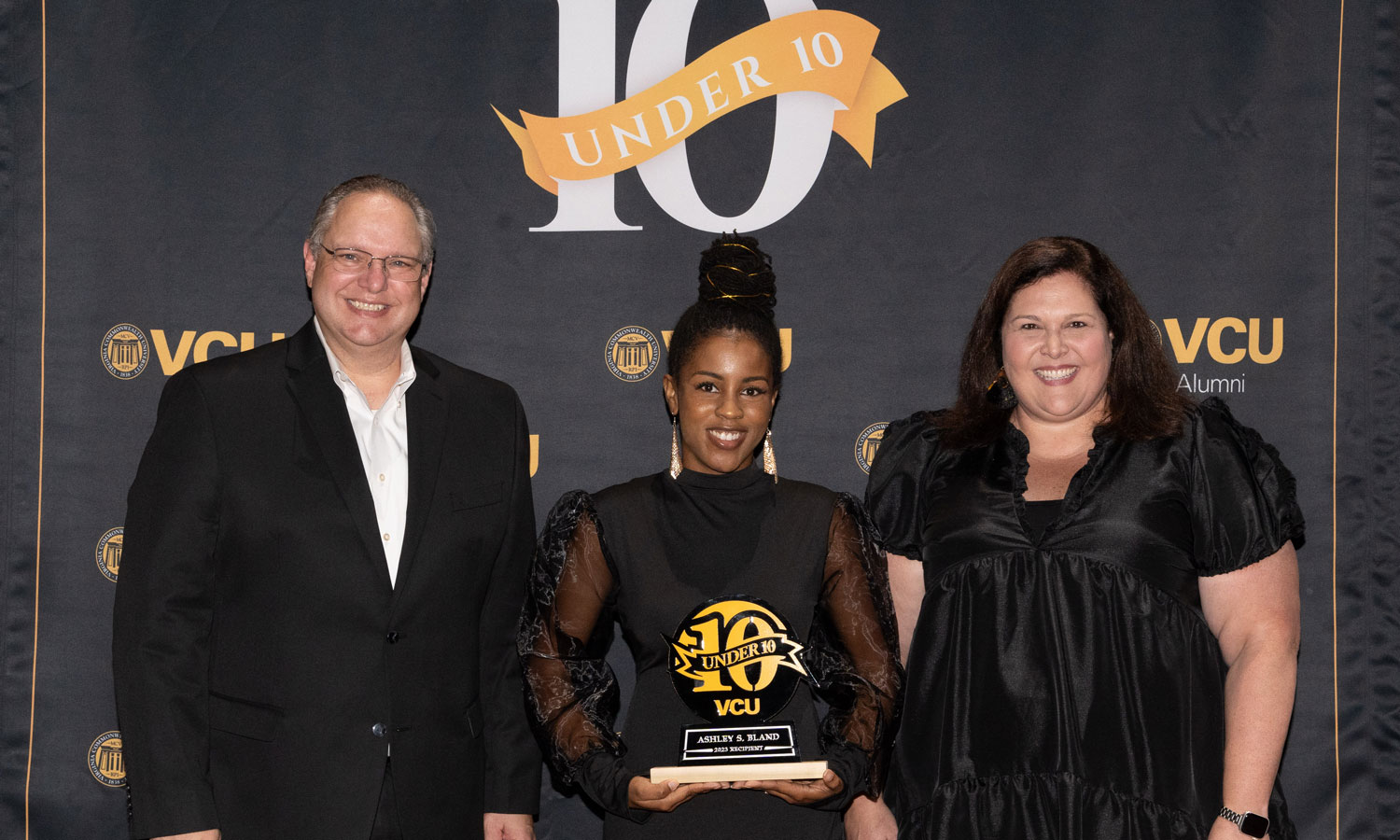 Ashley Bland (middle) is presented with VCU Alumni’s 10 Under 10 award by Jay Davenport, vice president of development and alumni relations, (left) and Elizabeth Bass, associate vice president for alumni relations (right).
