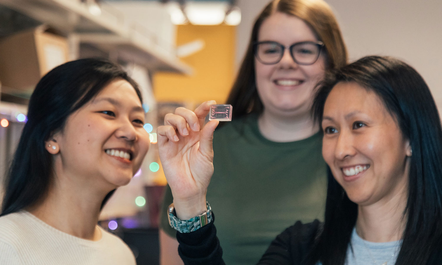 Priscilla Hwang Ph.D. (right) holds the “cancer-on-a-chip model,” a microfluidic model of breast cancer. With her are students Jessanne Lichtenberg (left) and Corinne Leonard (center)